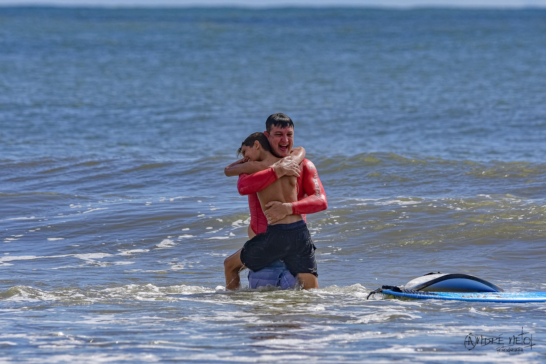 Pai e filho abraçados no mar, comemorando a primeira onda